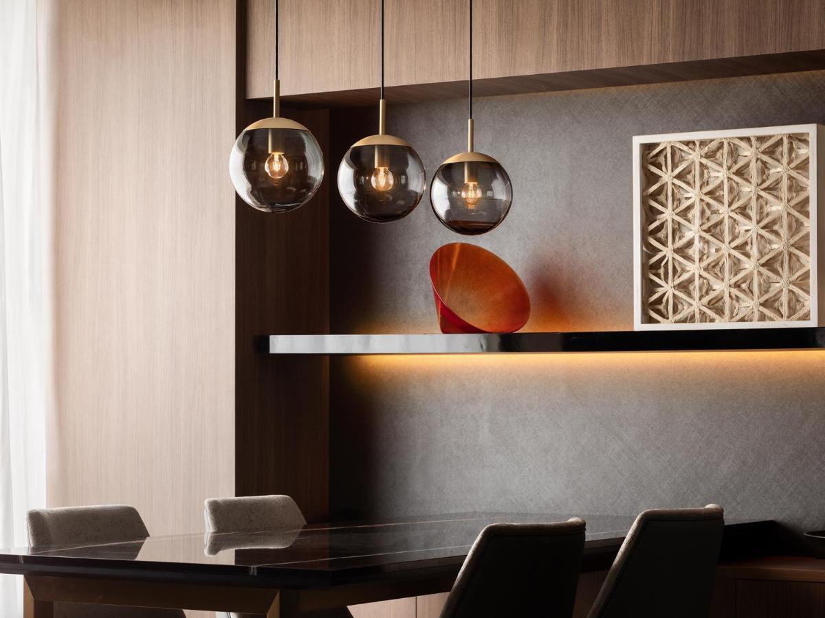 Mitsui Garden Hotel Roppongi Tokyo Premier Kültér fotó The photo depicts a modern interior design scene. It features a sleek dining area with a dark wooden table and comfortable chairs. Above the table, there are three pendant lights with glass shades that provide ambient lighting. A geometric art piece 