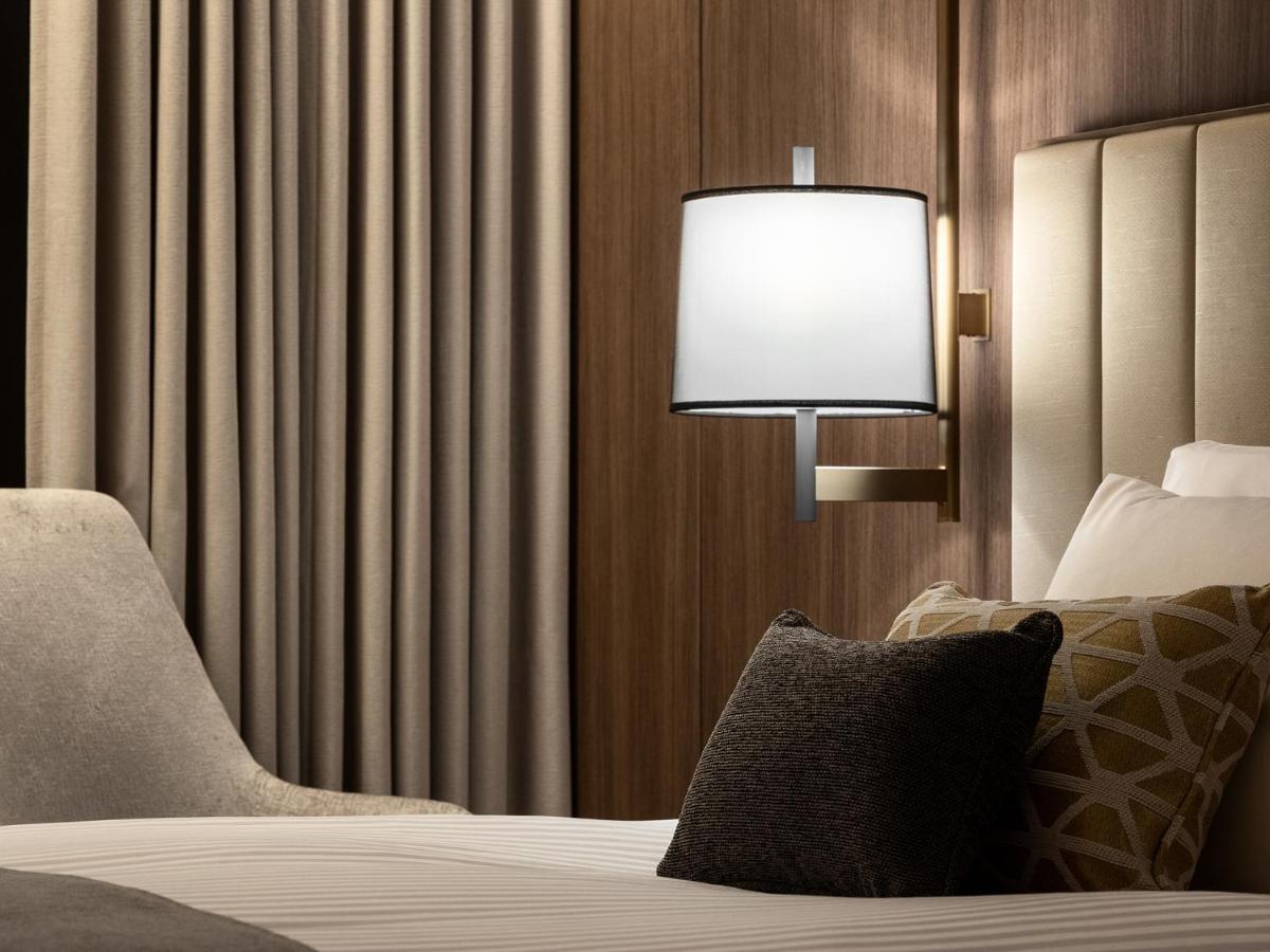 Mitsui Garden Hotel Roppongi Tokyo Premier Kültér fotó The photo displays a cozy hotel room setting. It features a neatly made bed with white linens and several decorative pillows. To the side, there’s a stylish bedside lamp mounted on the wall with a round white shade. Behind the lamp, there are elegant