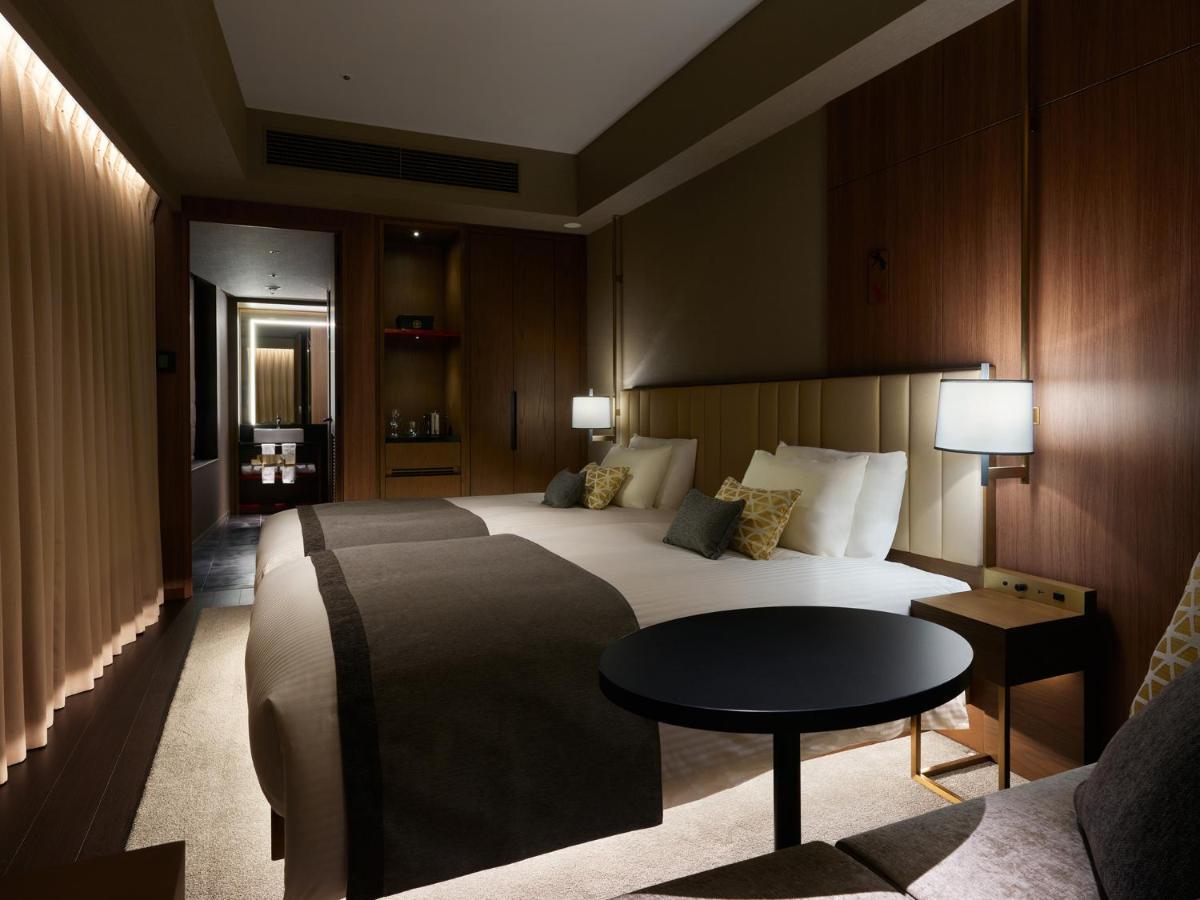 Mitsui Garden Hotel Roppongi Tokyo Premier Kültér fotó The photo shows a stylish hotel room featuring two beds with plush bedding and decorative pillows. The walls are made of wood, creating a warm and modern atmosphere. There are bedside lamps on each side of the beds providing soft lighting. A small ro