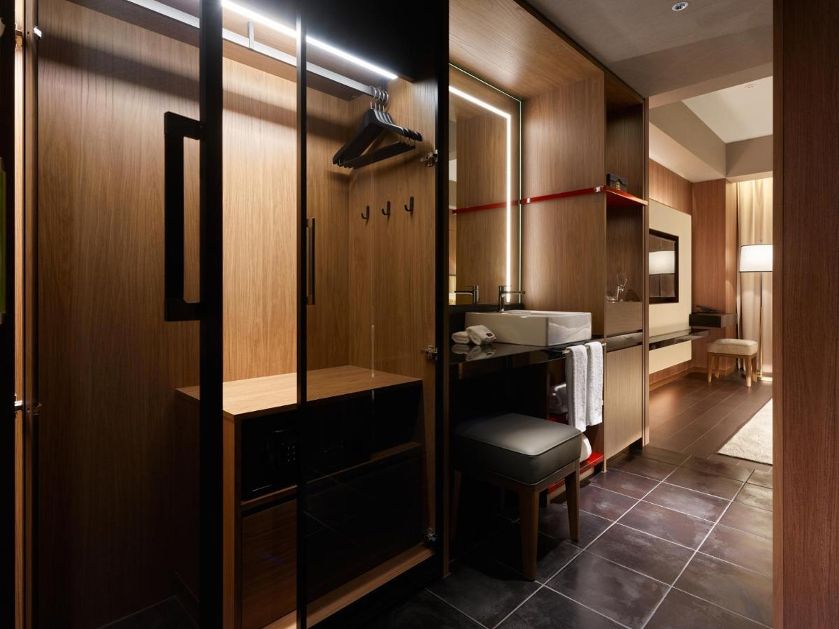 Mitsui Garden Hotel Roppongi Tokyo Premier Kültér fotó The photo depicts a modern and stylish hotel room's closet area. It features wooden cabinetry with a sleek finish, including mirrored doors. Inside, there are hangers for clothing and hooks mounted on the wall. A small bench or chair is positioned ne