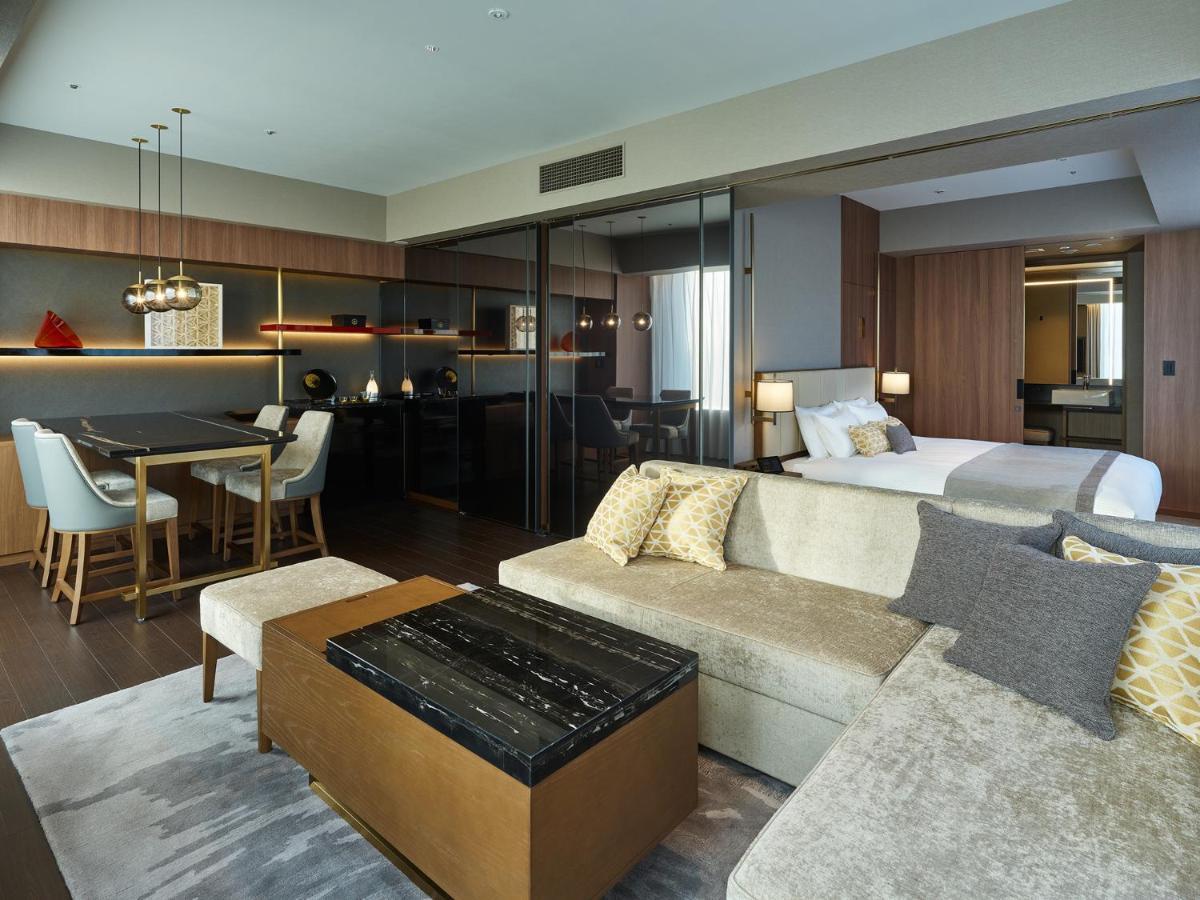 Mitsui Garden Hotel Roppongi Tokyo Premier Kültér fotó The image shows a modern hotel room or suite that features a contemporary design. Key elements include:

- A comfortable seating area with a light-colored sofa and a stylish coffee table.
- A dining area with a table and chairs, suggesting space for 