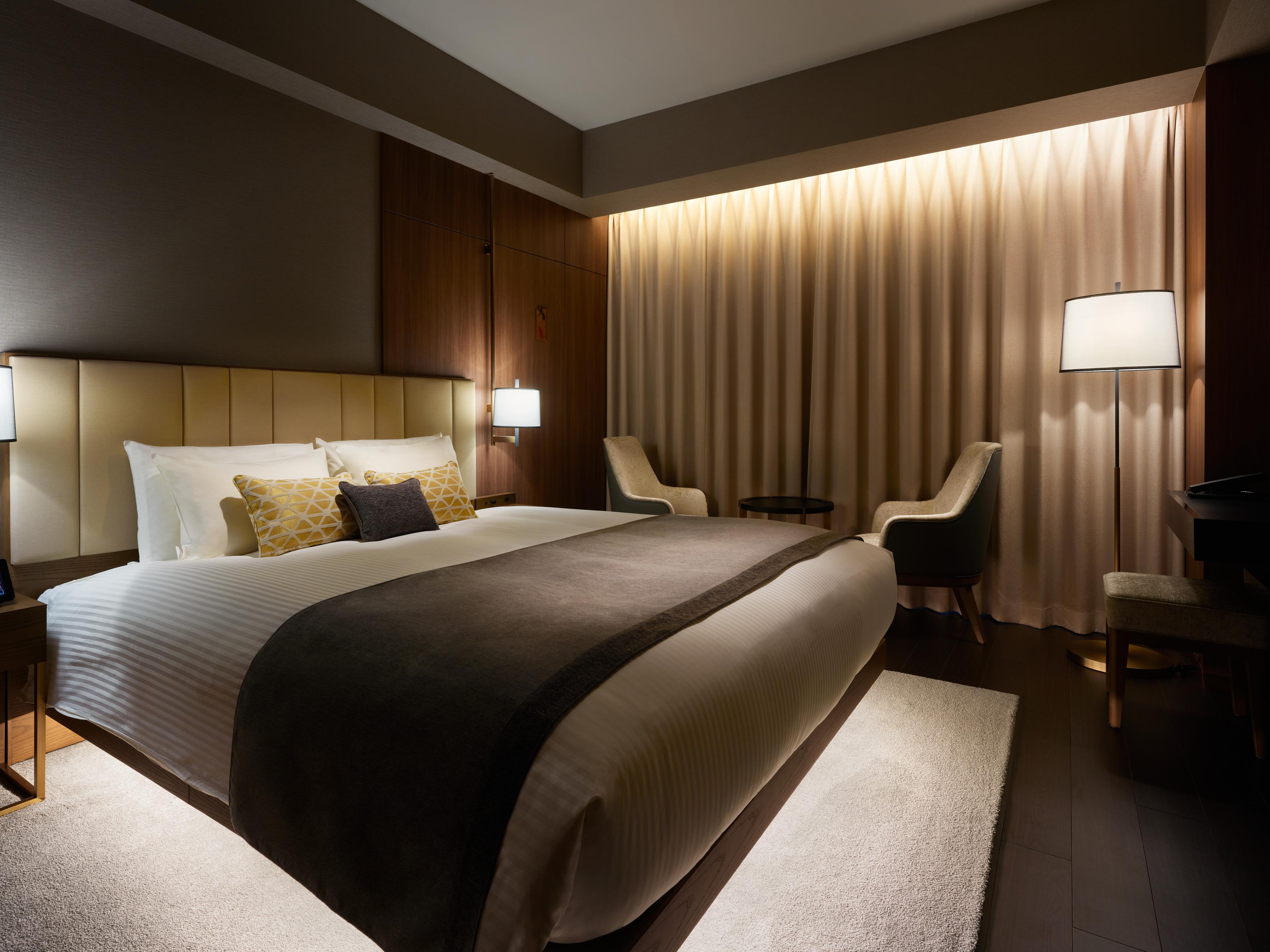 Mitsui Garden Hotel Roppongi Tokyo Premier Kültér fotó The photo depicts a modern hotel bedroom. It features a large bed with white linens and a dark gray throw blanket, accented by decorative pillows. The room has a warm ambiance created by soft lighting, including two bedside lamps and a lighted area b