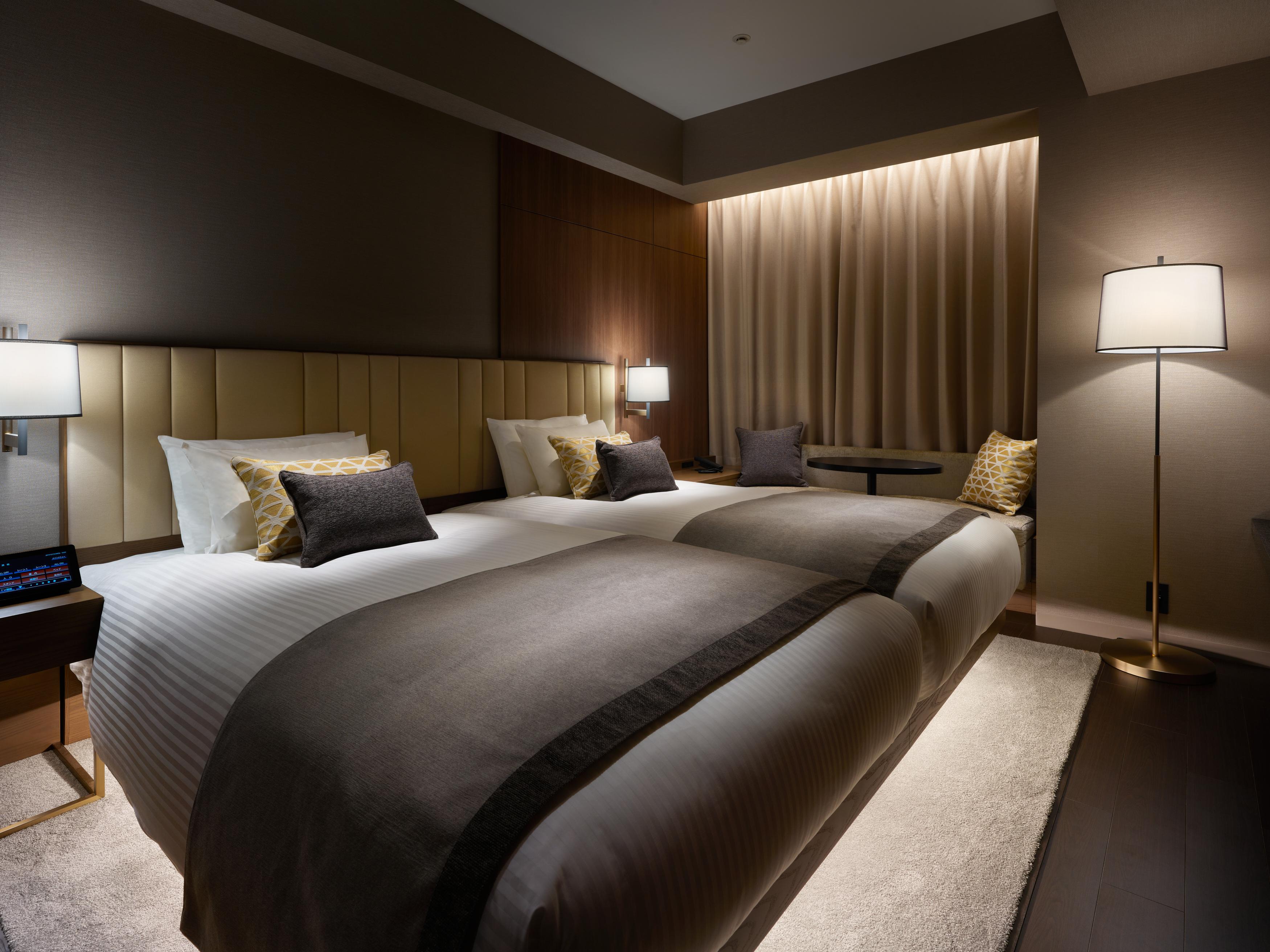 Mitsui Garden Hotel Roppongi Tokyo Premier Kültér fotó The photo shows a modern hotel room featuring two beds with elegant bedding in neutral colors. Each bed is adorned with decorative pillows. The room has a sophisticated ambiance with dim lighting, highlighted by table lamps on either side of the beds
