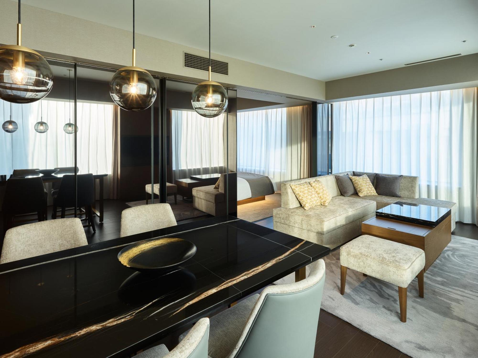 Mitsui Garden Hotel Roppongi Tokyo Premier Kültér fotó The photo shows a modern and stylish living area. It features a dining table with elegant chairs, a comfortable seating area with a light-colored sofa, and a coffee table. The room is well-lit by large windows draped with sheer curtains, allowing nat
