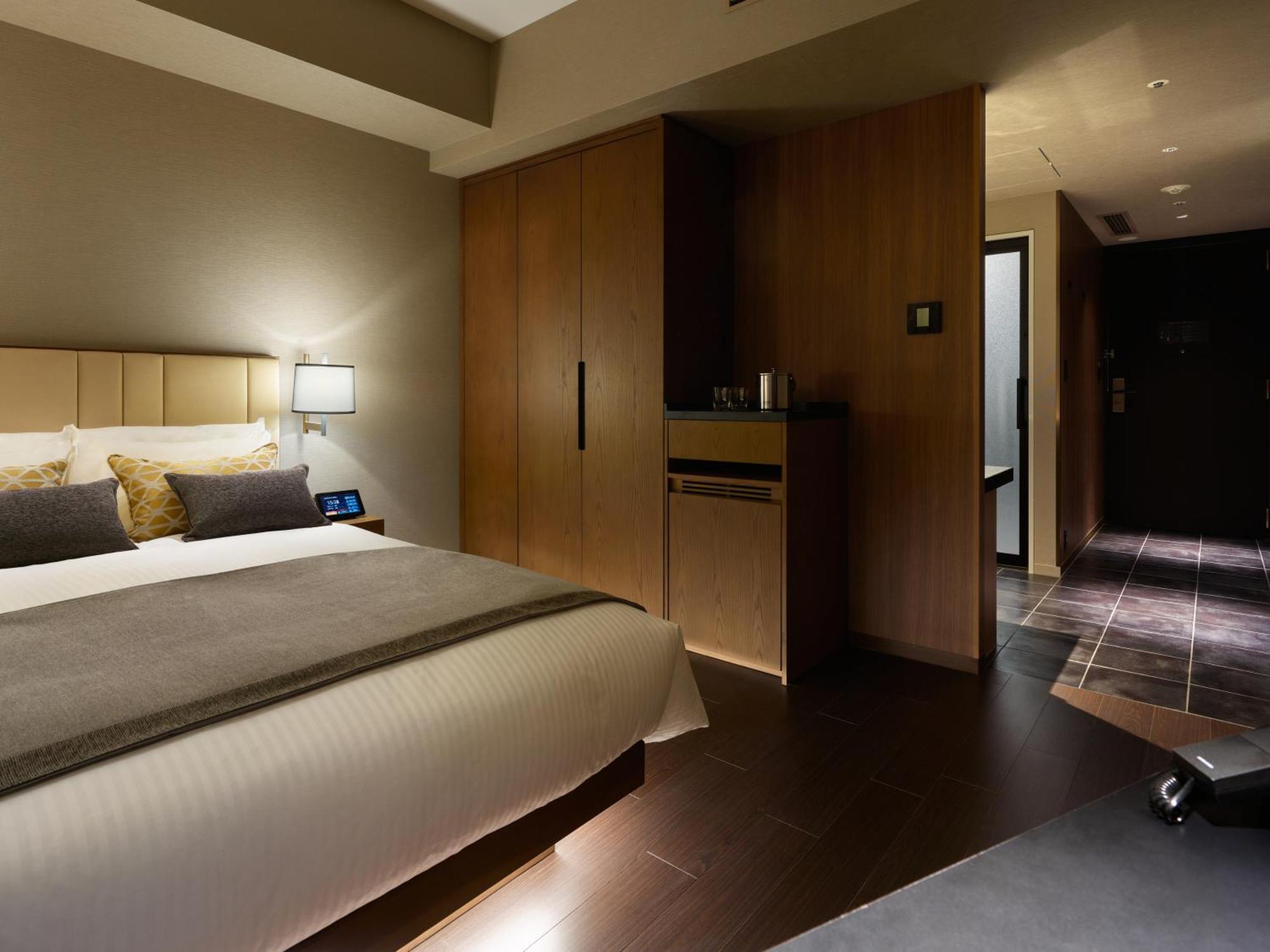 Mitsui Garden Hotel Roppongi Tokyo Premier Kültér fotó The photo shows a modern hotel room featuring a neatly made bed with decorative pillows. The room has wooden accents, including a wardrobe and cabinetry, contributing to a warm ambiance. A bedside lamp is on one side of the bed, and there's a small a