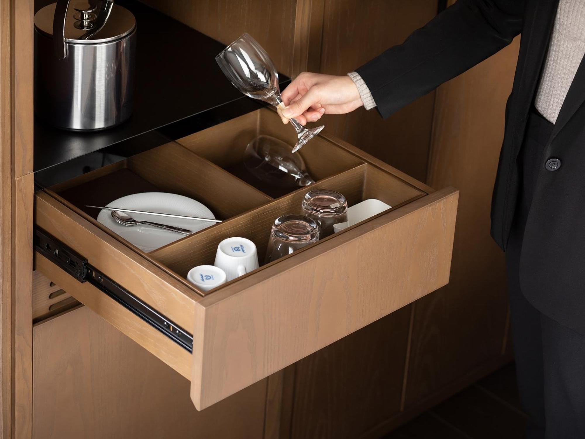 Mitsui Garden Hotel Roppongi Tokyo Premier Kültér fotó The photo depicts a wooden kitchen drawer being pulled open, revealing a neatly organized selection of dishware. Inside, there are glass cups, a wine glass being held by a person, and plates. The setting appears modern and sleek, with a sophisticated