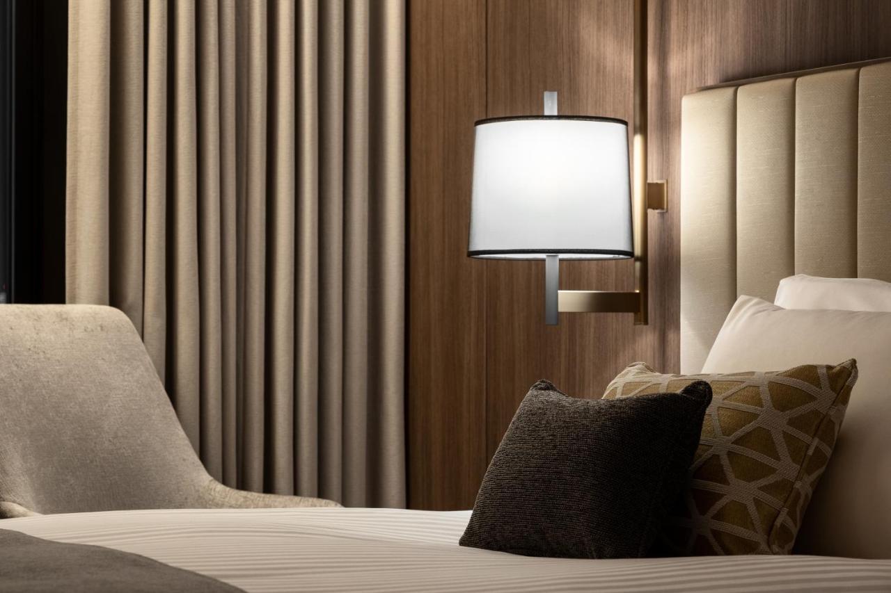Mitsui Garden Hotel Roppongi Tokyo Premier Kültér fotó The photo shows a cozy hotel bedroom setting. There is a neatly made bed with white linens and a few decorative pillows, including a dark one and another with a geometric pattern. To the side, there is a soft armchair and a modern wall lamp mounted a